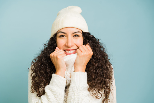 Happy young woman with curly hair feeling cheerful enjoying the winter weather wearing a knit hat and sweater smiling during the cold
