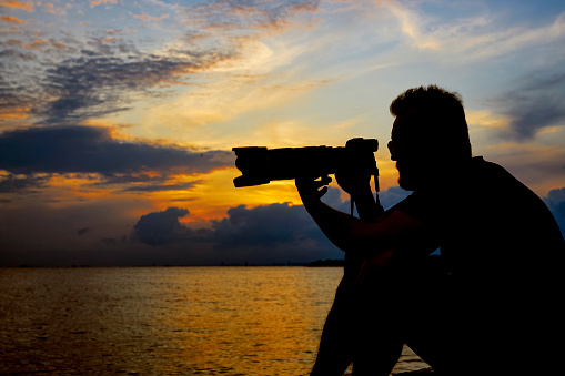 closeup silhouette of a male photographer with tele lens and dramatic sky with sea view