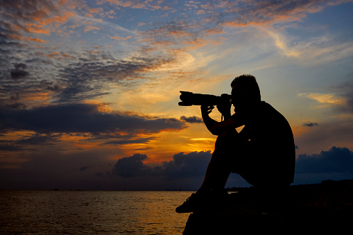 photographer sitting near seaside with dramatic sunset clouds