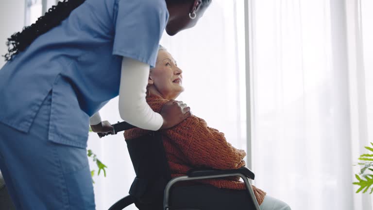 Senior woman, wheelchair and nurse by window, thinking and smile for help, support and care in retirement. Caregiver, nursing home and person with disability, patient and happy for rehabilitation