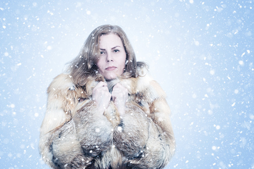 A woman in a fox fur coat without a hat, freezing in winter, snowing on a blue background