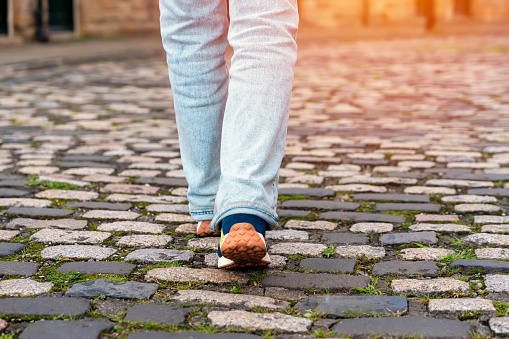 feet of a woman in jeans and a sneakers walking along a paved street on the city street