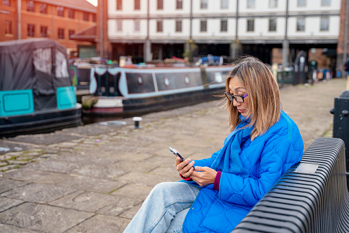 unhappy surprised asian woman in blue jacket and glasses walking on the quays, pier, sitting on bench, looking at yacht, sailboat, boat, talking by phone Lifestyle travel concept