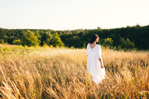 Brunette young woman in wild field. Natural beauty and romance concept. Sunset light. View from the back