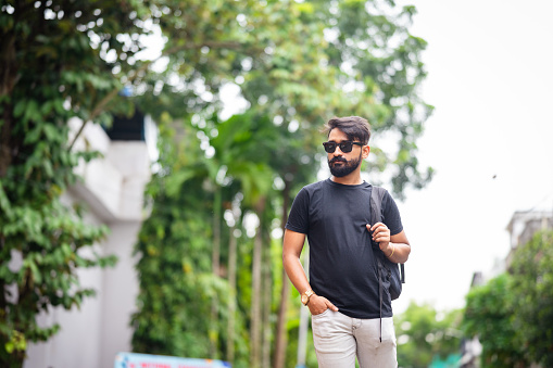 Charming young man wearing black T-Shirt and sunglasses walking in the city with a backpack