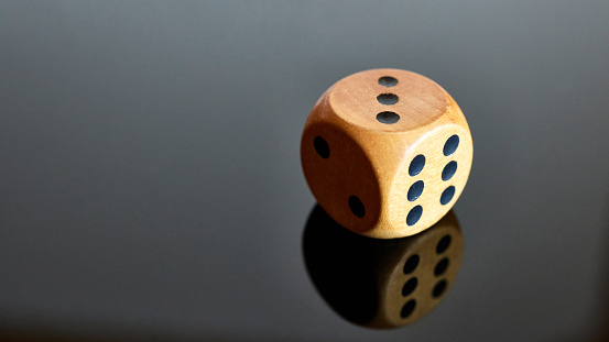A brown wooden dice with black dots lying on shiny black background