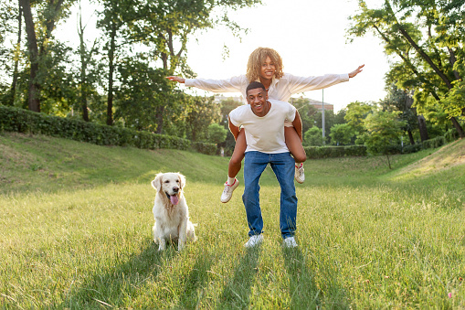 african american young couple in love runs with dog in the park in the summer and smiles