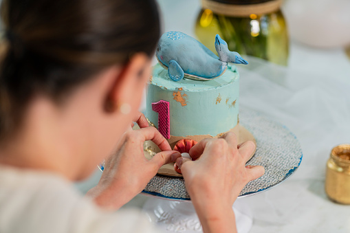 Latin woman with an average age of 35 years, a professional baker, is inside her kitchen where she prepares delicious cakes and makes a hand-painted design of a sea-themed cake.