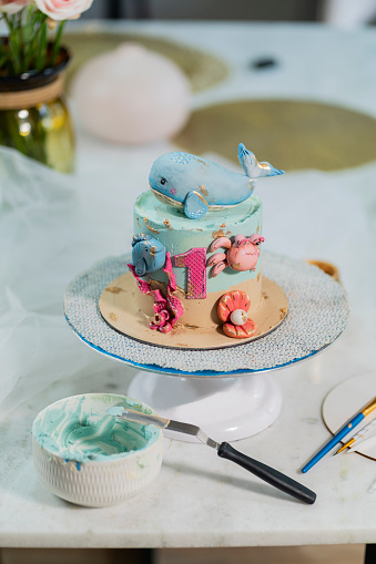 Latin woman with an average age of 35 years, a professional baker, is inside her kitchen where she prepares delicious cakes and makes a hand-painted design of a sea-themed cake.