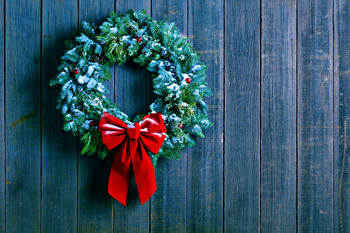 A Christmas wreath dusted with snow hangs from an old weathered wood wall of a barn.