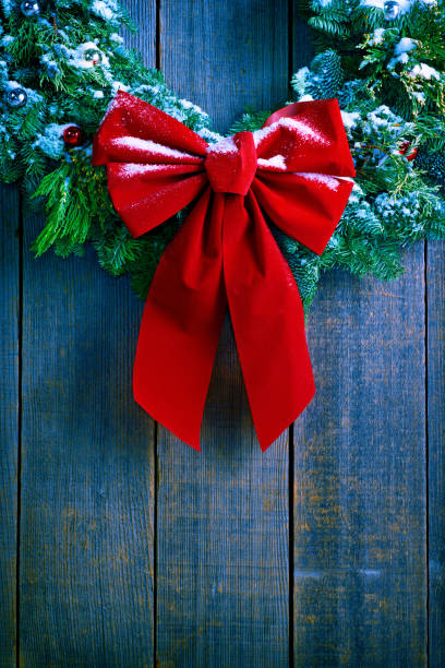 A Christmas wreath dusted with snow hangs from an old weathered wood wall of a barn.