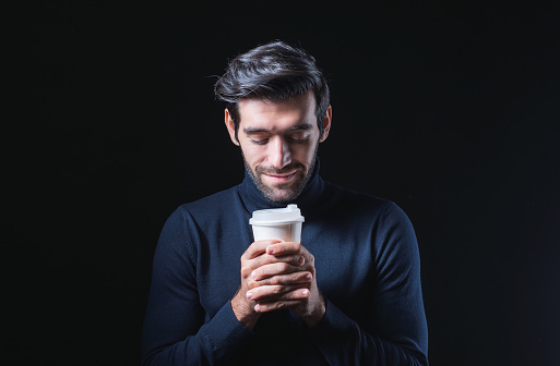 A young, white man is holding a cup of sweet tea or coffee that has blank space on it for your promotional text message or advertisement. Man with a mock-up of a white cup of coffee and a blue sweater
