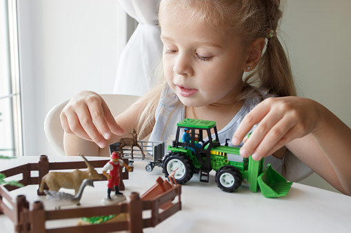 Cute child plays with farm equipment toys. Business or farming concept, blurred background