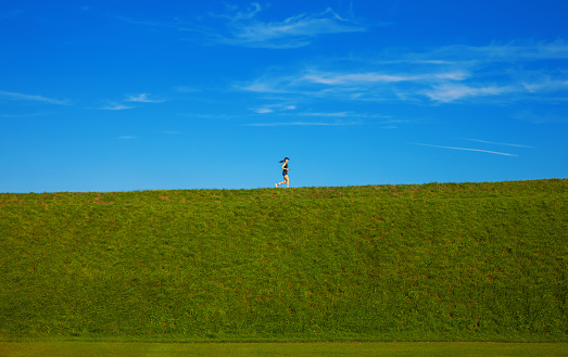 Woman runs uphill on a green meadow and clear blue sky on background\nSide view and lots of space around