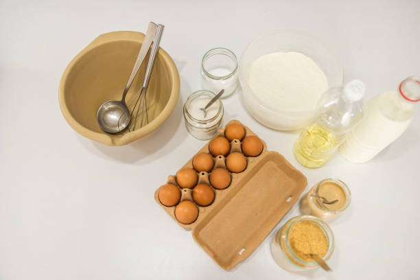 Ingredients for making pancake dough (eggs, flour, milk, sugar, salt, oil) on white wooden table.