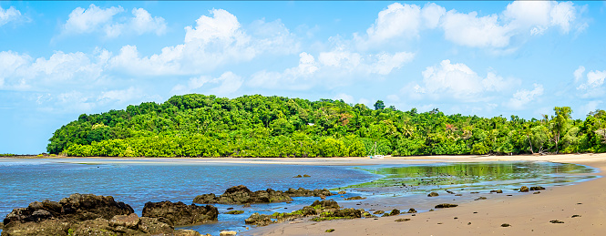 Exposed rocks at low tide together with the lush rainforest highlight an interesting panoramic vista at Mission Beach, tropical Queensland