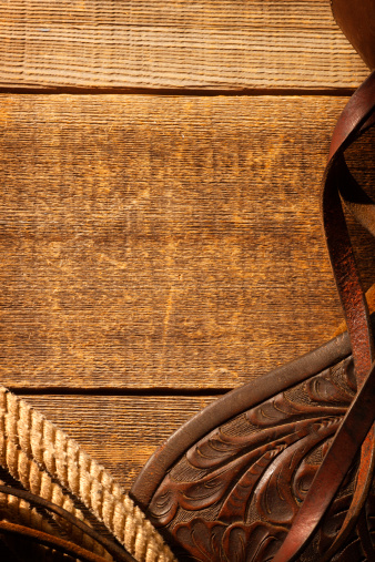Barn wood framed by lariat,saddle flap, and leather riding tack on weathered wood surface