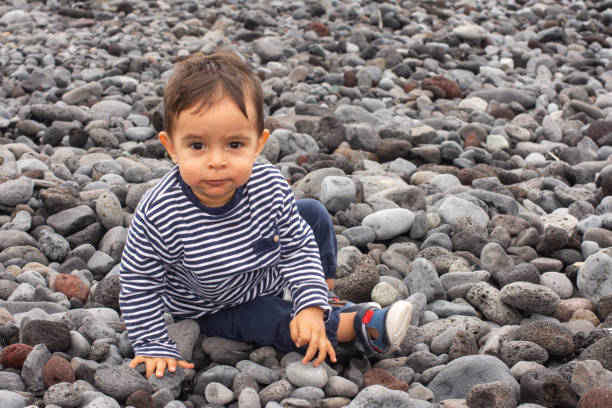 Baby sitting on the beach in blue clothes, playing with the stones