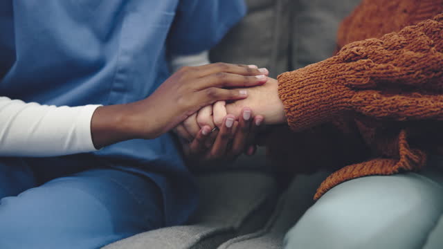 Nurse, woman and holding hands on sofa for support, helping and healthcare or homecare service. Caregiver, doctor and medical people with patient on couch for empathy, kindness and hands together