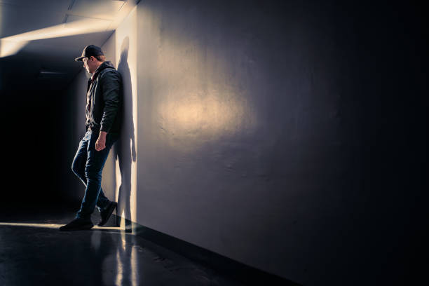 istock Serious sad man standing in dark corridor. Mystery guy in spotlight. Dramatic light and shadow. Stalker or outcast. Person waiting, hiding, sneaking or eavesdropping. 1731744612