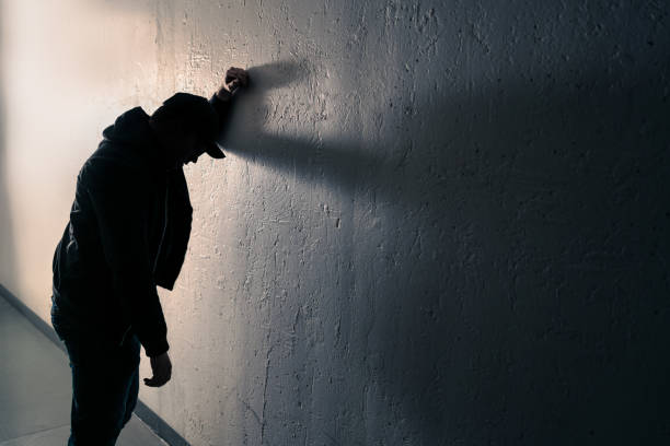 Drunk, intoxicated man against wall. Alcohol problem, drug addiction or overdose concept. Nauseous, vomit on street. Young dizzy person in dark alley. Sick drunkard. Liver disease. stock photo