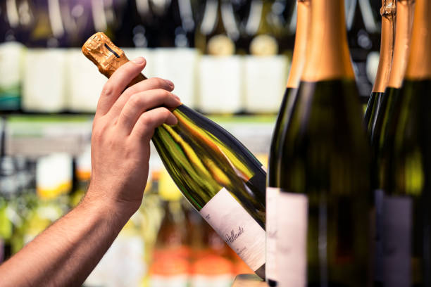 Sparkling wine from shelf of alcohol store. Bottle in hand. Liquor shop. Prosecco or champagne display in spirits market or supermarket. Man buying expensive drink. stock photo