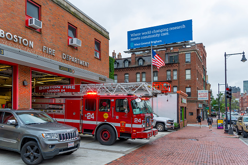 Fire Station in Boston, Massachusetts, USA.  There are pedestrians on the sidewalk and a fire engine driving out of the garage.