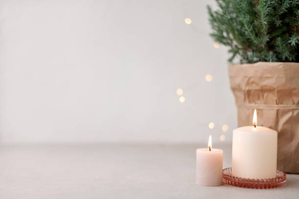 istock Candles and blurred defocused garland lights, juniper in pot on beige table and empty white wall background. Aesthetic Scandinavian Christmas home decoration, interior design template 1731778253