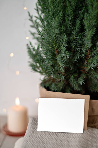 istock Blank paper card mockup, envelope, sweaters, blurred defocused candle and garland lights, juniper in pot. Cozy winter minimal invitation or postcard design template, Scandinavian home interior 1731778800