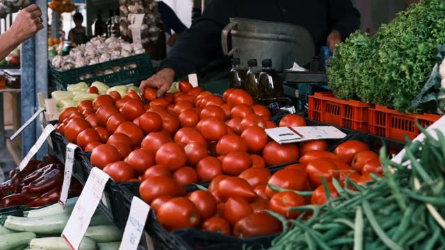 4K or Hd shot of a scene at market stand: a female client buyer hand shows tomatoes that wants to buy  to man seller that takes product and puts in the bag.