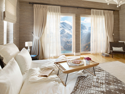 Wide angle shot of a comfortable bedroom and breakfast tray with image montaged Alp mountains