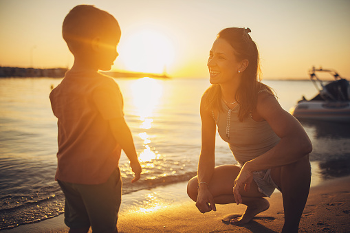 Woman with her little son on the beach by the sea in sunset, they are on vacation.