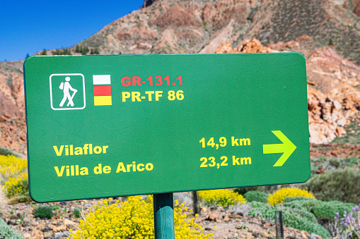 Cañadas del Teide, Tenerife, Spain; April 20 2023:  Vilaflor and Villa de Arico trail signaling sign, with sunlight, mountain and blue sky background, Teide national park, Canary islands
