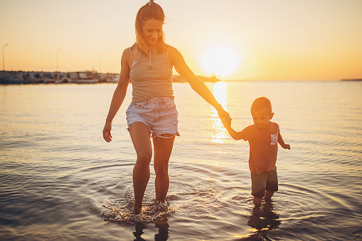 Woman with her little son in shallow sea in sunset, they are on vacation.