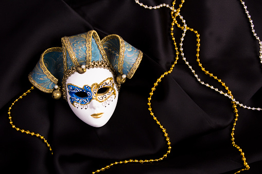 Venetian carnival mask and garland on the black textile background. Top view. Close-up. Holiday background.