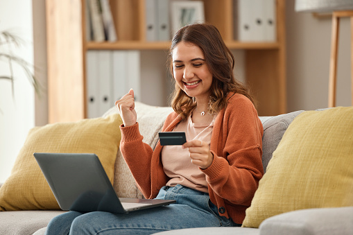 Excited, woman and laptop with credit card, banking and online shopping with fintech, transaction and happiness in a lounge. Person, home and girl on a couch, pc and celebration with payment or bonus