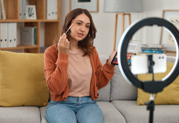 istock Social media, makeup and tutorial with a woman influencer in her home to broadcast live content to viewers. Streaming, product or review with a young brand ambassador in the living room for cosmetics 1731851698
