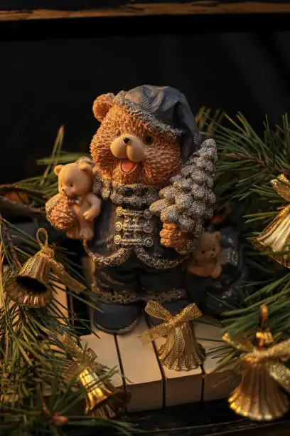 Photo of Decorative figurine of a bear with a Christmas tree on a piano, decorated with a pine tree and bells. Festive new year decor, warm dark composition