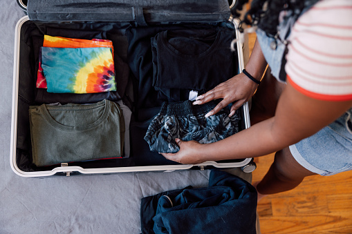 Young woman in bedroom packing suitcase for holidays.