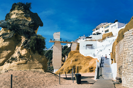 rear view on woman going up  stairs on praia dos pescadores  in Albufeira –  Portugal at sunrise hour, elevator in the background