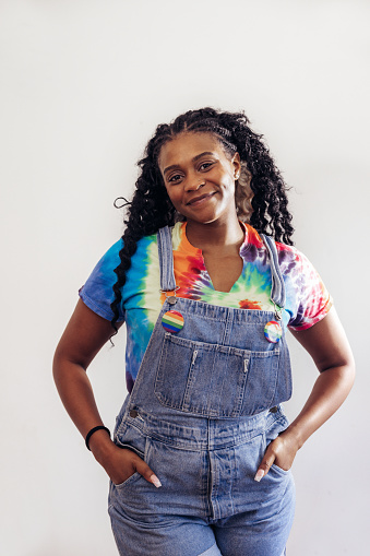 Woman with a tie dye t-shirt and LGBTQ+ friendly pins posing for a portrait on white background.