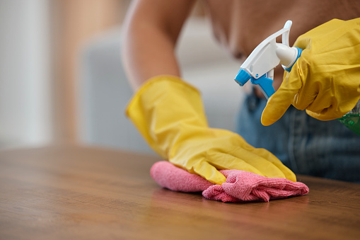 Person, hands and spray bottle in cleaning or housekeeping on table for hygiene or disinfection at home. Closeup of domestic, maid or cleaner wiping furniture or desk for bacteria or germ removal