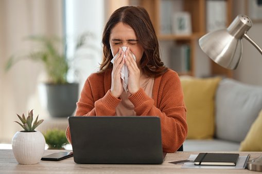 Woman, blowing nose and student with laptop, allergies or burnout with virus, fatigue and sick with sinus infection. Toilet paper, health fail and overworked with university assessment while at home
