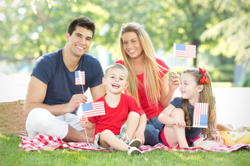 Parents with cute little children enjoying July 4th picnic, holding american flags.