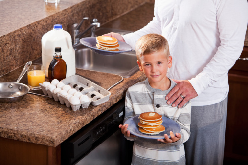 Little boy (6 years) in kitchen with father (40s), having pancakes for breakfast.