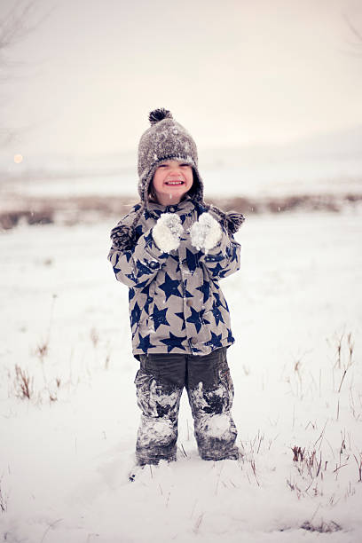 Cute little boy in winter clothes enjoying the first snow. It is almost the end of the day and it is very cold outside, but nevertheless he looks very happy and cheerful. Vintage look.