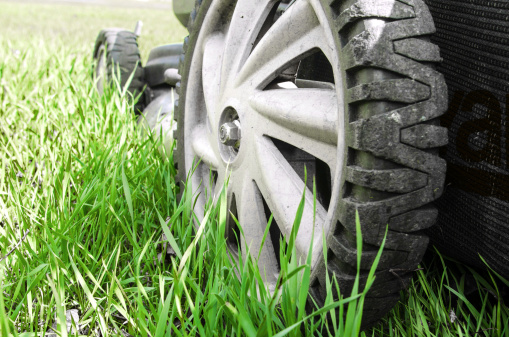 The wheels of a used lawn mower on grass that requires cutting.