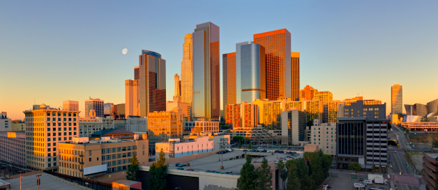 High angle panoramic view of downtown Los Angeles shortly after sunrise, with the moon preparing to set behind the skyline. 
