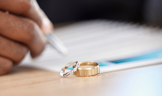 Divorce, rings and signature on paperwork for a lawyer, register wedding or writing on a contract. Table, closeup and a certificate, planning or legal documrnts for a commitment or engagement