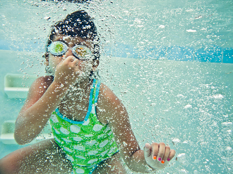 Little girl swimming underwater wearing goggles.